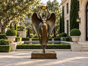 Bronze winged goddess statue holding a golden sphere in a luxury European-style estate garden
