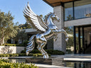 Mirror-polished stainless steel Pegasus sculpture with reflective wings displayed outside a modern luxury villa beside a reflecting pool.