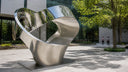 Mirror and satin stainless steel sculpture installed in a contemporary architectural courtyard