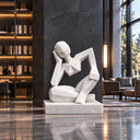 An abstract matte white stone statue featuring a seated curled pose, crafted specifically for contemporary art gallery interiors.