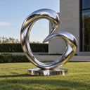 Mirror-polished abstract stainless steel sculpture on a manicured lawn beside modern architecture