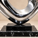 Detailed view of the polished stainless steel sculpture's lower curved junction and black marble pedestal.