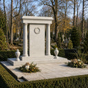 Framed by autumn foliage and fallen leaves, this cream-colored granite memorial arch stands as a dignified tribute, complete with a circular wreath design and a structured base.