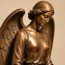 Close-up of a bronze angel sculpture showing its serene facial expression, braided hair, flowing robe and sculpted wings.
