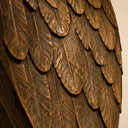 Close-up of layered feather carvings on a bronze angel sculpture, showing the textured wing surface and antique bronze finish.