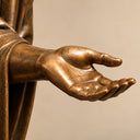 Detailed view of the bronze angel statue's open palm and extended hand, highlighting the sculpted fingers and warm bronze patina.