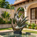 Distinguished by a curved neck and sweeping feather forms, this abstract bronze bird sculpture pairs warm metallic highlights with green accents beside a villa garden pool.