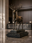 Large bronze deer sculpture displayed on a black marble pedestal in a modern luxury lobby