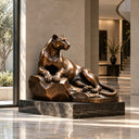 Bronze reclining lioness sculpture resting on a rock, placed in a luxury modern lobby with marble floors and glass windows, ideal for high-end indoor art decoration and interior design.