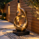 A bronze ribbon sculpture joins sweeping gold curves around an open center, creating a flame-like focal point for a landscaped garden.