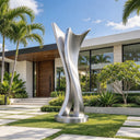 Composed of three ascending forms, this brushed stainless steel garden sculpture rises from a circular base, defining a modern focal point for a luxury villa entrance.