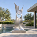 Brushed stainless steel abstract heart sculpture with twin vertical forms displayed beside a luxury villa swimming pool