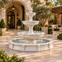 Carved stone fountain water feature surrounded by flowers in a sunny garden courtyard, perfect for luxury outdoor landscape design and residential patio decoration.