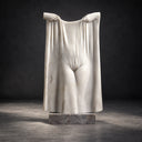 Rendered against a dark backdrop, this carved white marble drapery artwork accentuates the dramatic folds and hands of the surreal stone figure, staged for fine art gallery catalogs.