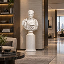 Classical white marble Caesar bust displayed on a tall white pedestal in a modern luxury lobby with contemporary furniture and warm lighting, suitable for high-end interior decoration and art display.

