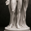 Close-up of a white marble statue lower body and draped robe on a dark background, showcasing fine carving texture and pedestal details for product display.
