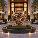 Contemporary bronze ribbon sculpture displayed at a modern indoor lobby entrance with warm lighting and greenery, suitable for high-end interior art decor and commercial space design.