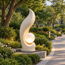 Sculpted as a flowing wave, this Egyptian Beige marble landscape light sculpture incorporates a glowing spherical lamp, installed along a garden pathway.
