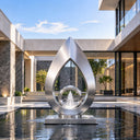 Positioned within a reflecting pool, this contemporary stainless steel fountain sculpture combines a teardrop outline with a central circle, defining a serene courtyard water feature.