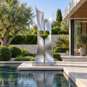 Formed by two curved stainless steel columns, this contemporary heart sculpture creates a central hollow silhouette, enhancing a luxury villa garden setting.