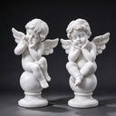 Studio product shot of a pair of white marble cupid statues sitting on round globes against a solid black background.