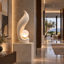 Crafted with a smooth organic curve, this contemporary garden lighting sculpture contains an illuminated sphere, placed within a modern lobby corridor.