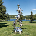 Intertwining in a spiraling pod, this large metal dolphin statue inhabits a serene botanical setting, its mirror-finish reflecting the surrounding landscape.