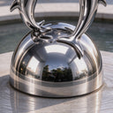 Flourishing from a symmetrical domed pedestal, this large metal dolphin statue features a smooth mirror finish at its structural anchor.