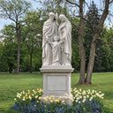 Large white marble Holy Family statue of Jesus, Mary, and Joseph displayed on a stone pedestal in a landscaped outdoor garden.
