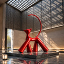 Large glossy red modern cat sculpture displayed on a black marble pedestal in a luxury hotel atrium with a geometric skylight.