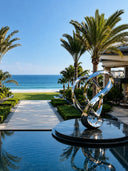 Polished stainless steel abstract sculpture in a luxury seaside resort landscape.