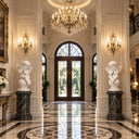 Two white marble cupid statues positioned inside a grand hall with a chandelier and polished marble floor, reflecting classical architecture.