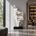 Minimalist white art sculpture placed in front of a grey wall near a window, with natural light highlighting its flowing design, perfect for modern home or office decoration.