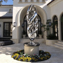 Mirror polished abstract stainless steel sculpture with intricate intertwined metal forms displayed at the entrance of a luxury Mediterranean villa.