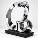 Mirror-polished abstract stainless steel loop sculpture with folded ribbon curves and a black metal base.