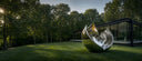 Mirror polished stainless steel sculpture displayed on the lawn of a modern woodland estate