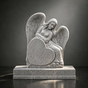 MM-005 angel memorial stone sculpture detail showing carved wings, facial features, heart-shaped plaque, and natural gray stone texture