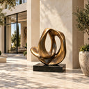 Modern abstract bronze loop sculpture with a smooth organic shape on a black base, placed in a luxury outdoor courtyard with modern architecture and potted olive trees, ideal for high-end landscape decoration.