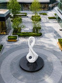 Modern abstract white sculpture displayed in a landscaped outdoor plaza with contemporary architecture