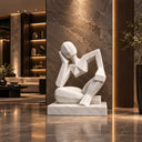 A modern geometric white alabaster sculpture depicting a seated thinking figure, designed as a striking art piece for luxury hotel lobbies.