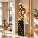 Presenting organic curves and a golden metallic finish, this modern bronze interior artwork is positioned near a home entrance to accent the foyer.