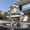 Modern outdoor abstract metal sculpture with reflective stainless steel curves installed beside a contemporary commercial building.