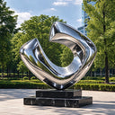 Modern outdoor abstract metal sculpture with reflective stainless steel curves installed in a landscaped commercial plaza.