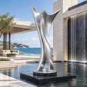 Standing beside a water feature, this modern outdoor metal sculpture showcases flowing vertical lines, curated as custom stainless steel artwork for a hotel courtyard.