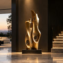 Tall modern abstract bronze sculpture with organic cutouts on a black base, placed in a luxury modern interior near a staircase at sunset, ideal for high-end floor decoration and contemporary art display.
