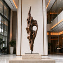 A narrow organic bronze sculpture with a large open void stands on a stone plinth inside a luxury foyer, formed through traditional lost-wax bronze casting. Model BB-034.