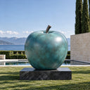 Serving as an iconic landmark, this outdoor bronze apple statue features a green patina and rests on a stone plinth within a university campus.