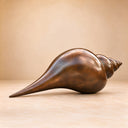 An outdoor conch shell statue cast in solid bronze, emphasizing the polished texture and pointed spiral tip against a studio backdrop for product catalogs.