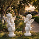 Two hand-carved white marble cupid statues seated directly on polished stone globes along a garden pathway, featuring mirrored poses.