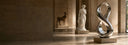 Large polished stainless steel infinity sculpture displayed in a grand gallery with classical statues